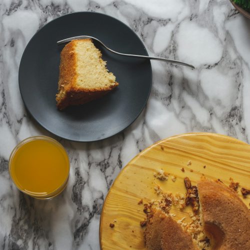 Fatia de bolo de arroz em prato escuro ao lado do bolo redondo com furo