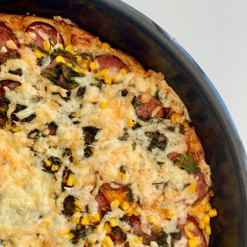 Pizza caseira de calabresa com queijo, milho e ervas numa fôrma redonda